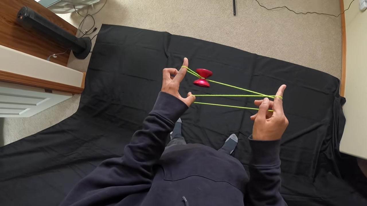 Hands guiding an orange yo-yo through a string formation.
